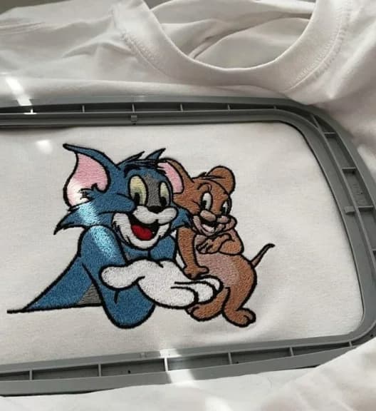 Tom and Jerry embroidery stitched on white fabric in a hoop